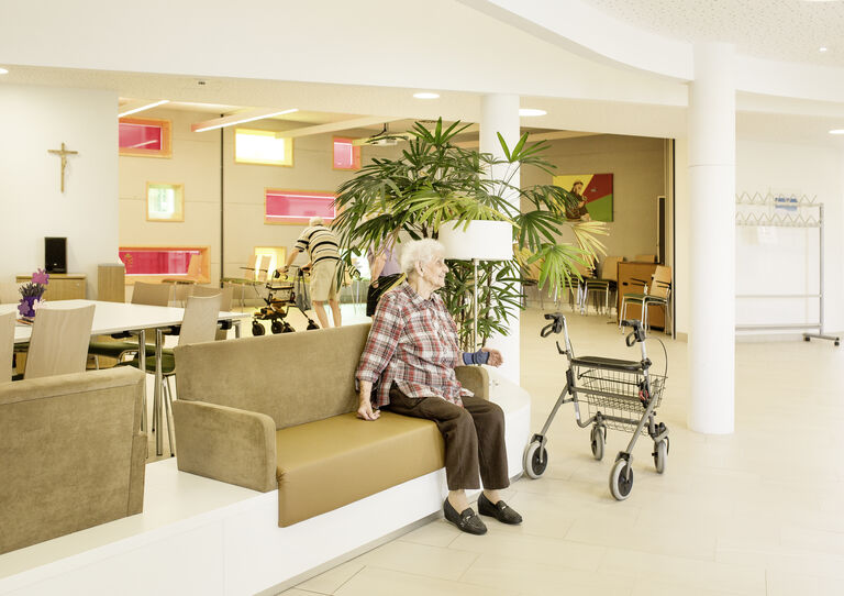 Eine Bewohnerin sitzt lächelnd vor der Kapelle des Urbanusheims.