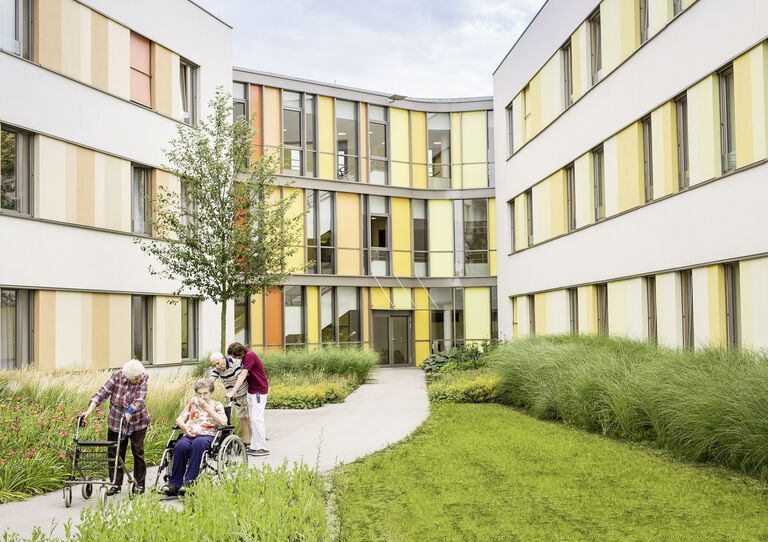 Ein Pfleger geht mit zwei Bewohnerinnen und einem Bewohner im Garten spazieren.