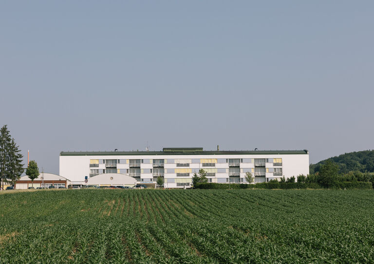 Außenansicht des Gebäudes, im Vordergrund ein blühender Acker.
