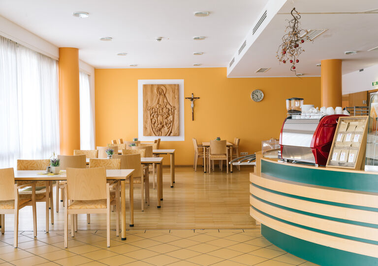 Die helle Cafeteria des Clementinums mit Holztischen und einer lindgrünen Theke.