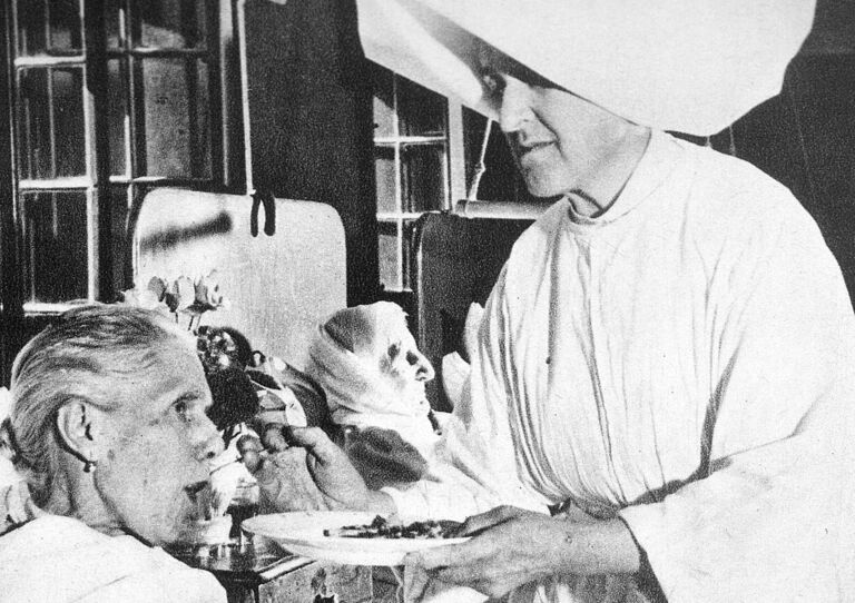 Eine Schwester füttert eine Patientin, die im Bett liegt.