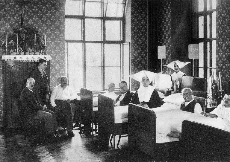 Ein historisches Krankenzimmer: Patienten in Betten und die betreuenden Schwestern.